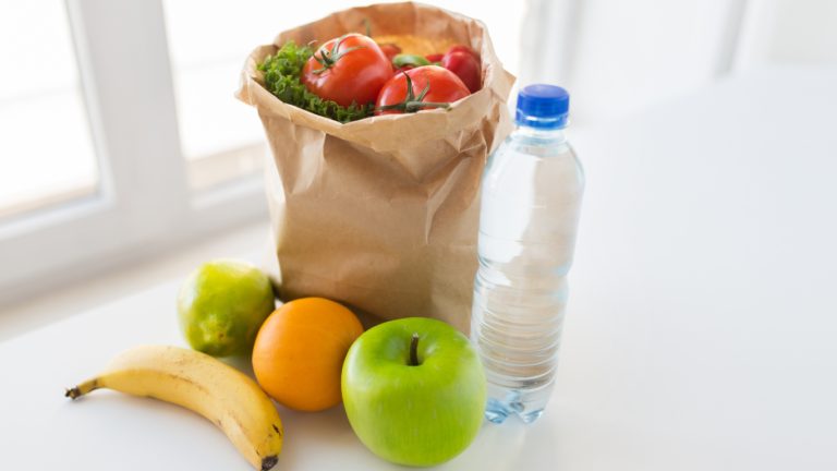 A plastic bag with fruits and vegetables with a bottle of water on a table