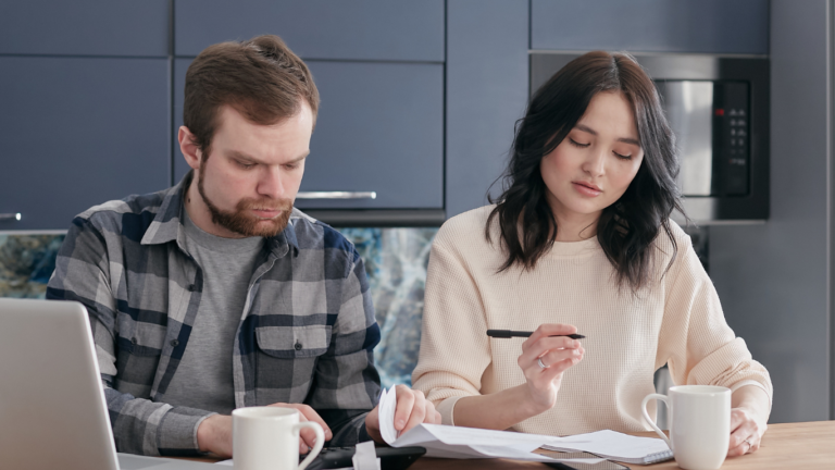 Man and woman sitting in the kitchen counter doing math with paper and a calculator